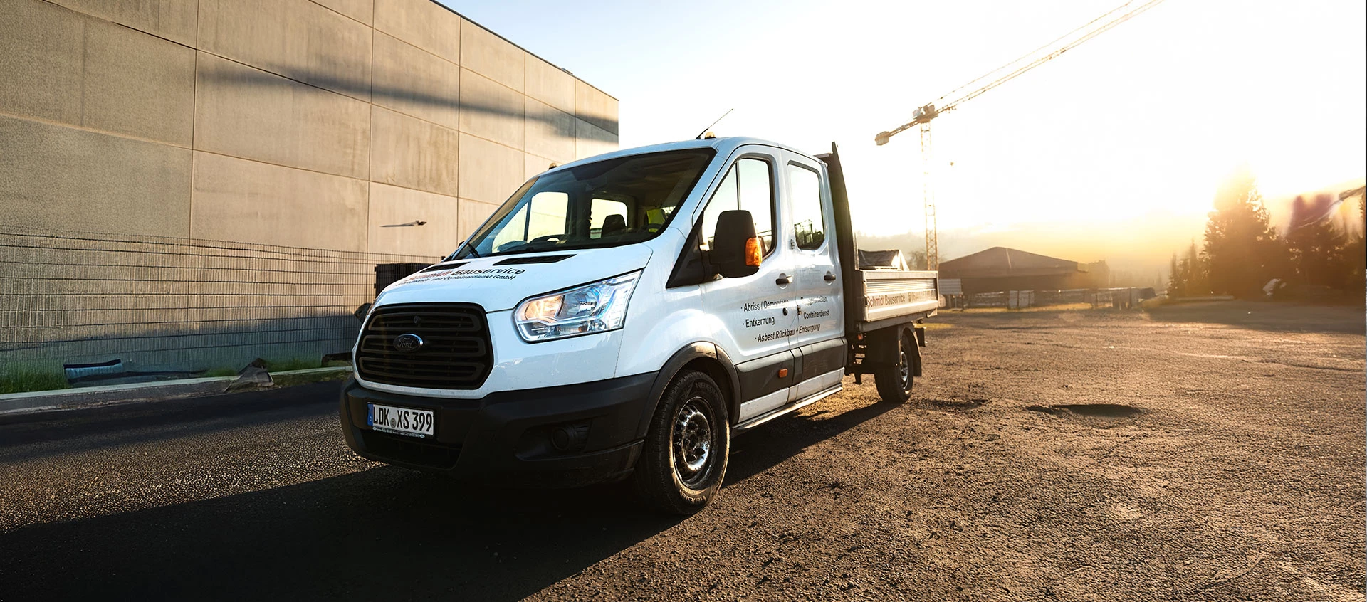 Ein weißer Transporter mit Ladefläche. Die Sonne scheint hell.